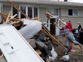 Lynn Eaton-Jones carries water-soaked wood to a huge pile of debris as she helps a friend gut the basement of a flooded home on Rue des Macons in the Pierrefonds district of Montreal on Saturday May 13, 2017.