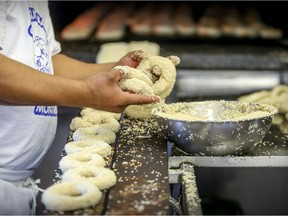 Baker Pedro Benitez dips bagels in bowl of sesame seeds before putting them in the oven at St. Viateur Bagel Shop in Montreal Monday May 15, 2017.