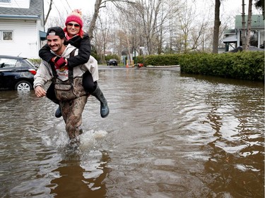 Jonathan Robert carries Jasmine King through a deeply flooded street as the Rivière des Prairies rises flooding Île-Mercier in Montreal on Wednesday May 3, 2017.