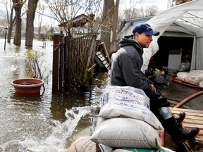 Marvin Solito sits on a sandbag wall monitoring the water levels as the Rivière des Prairies rises flooding Île-Mercier in Montreal on Wednesday May 3, 2017. Solito hasn't sleep since 2 a.m. and has 6 pumps running to keep the water at bay.