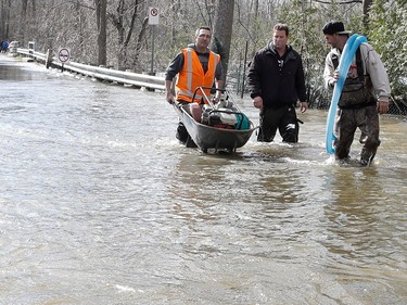 Volunteers use a wheelbarrow to shuttle a pump and gas as the Rivière des Prairies rises flooding Île-Mercier in Montreal on Wednesday May 3, 2017.