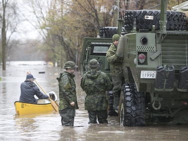 A man in a canoe paddles by Canadian military personnel next to their TAPV, on the flooded avenue du Chateau-Pierrefonds in Montreal on Sunday May 7, 2017. (Pierre Obendrauf / MONTREAL GAZETTE)