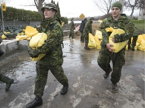 Canadian military personnel from the Fusillier Mont Royal in Montreal carry sand bags on Bouchard St. in Pierrefonds on Sunday, May 7, 2017.