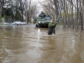 A member of the Van Doos leads an armoured personnel carrier through  flooded streets of Terrasse-Vaudreuil on Monday.