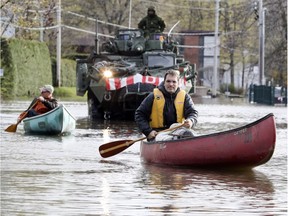 Alain Leroux, right, and Bernard Bégin paddle their canoes to pick up supplies on Blvd. du Lac in Deux-Montagnes, northwest of Montreal as Canadian army personnel deliver sandbags Monday May 8, 2017.