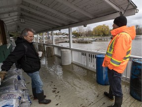 Pointe Claire Yacht Club manager Trevor Collins, wearing orange, and Barry Barnett stand near filled water barrels holding down the clubhouse deck.