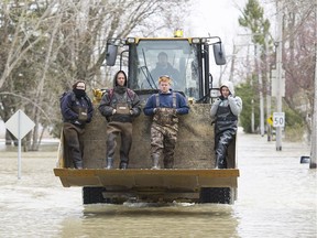 People are given a ride in a backhoe as they make their way home along a flooded street in Rigaud on Monday, May 8, 2017.