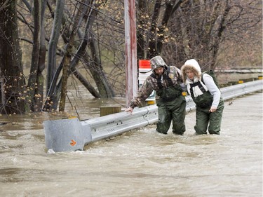 Residents brace themselves against the current as they cross the flooded bridge to the Île-Mercier district of Île-Bizard, Que. Friday, May 5,2017. Forecasts are calling for several more days of rain. THE CANADIAN PRESS/Ryan Remiorz