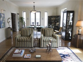 A view of the spacious, light-filled living/dining room in Emile Saleh's downtown condo. At one end is a pale green, glass-topped dining table, which reflects the light from a nearby window. On the other side of the room are armchairs covered with olive-green and cream striped upholstery.