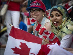 Vanessa Reginato, left, and Sabiha Begum sit on the sidewalk as they enjoy the Canada Day Parade in Montreal on Friday, July 1, 2016.