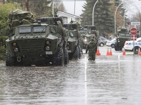 Military vehicles pull out of a flooded street in Pierrefonds on May 7.
