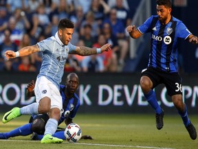 Kansas City Sporting forward Dom Dwyer (14) kicks the ball as Montreal Impact's Hassoun Camara and midfielder Marco Donadel (33) defend in the first half at Children's Mercy Park in Kansas City.