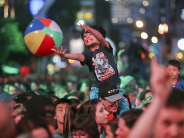 A young boys sitting on his father's shoulders reaches for a beach ball being batted around in the crowd before Walk Off the Earth outdoor blowout concert at the Montreal International Jazz Festival in Montreal Tuesday July 4, 2017.