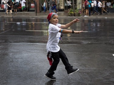 A young boy braves the rain to dance alone on Ste-Catherine street as he waits between floats during the annual Carifiesta parade in Montreal on Saturday July 8, 2017.