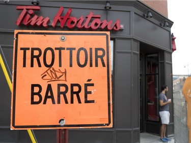 A Tim Hortons customer watches the ongoing construction on Notre-Dame Street in the Sud-Ouest district despite a sign announcing the sidewalk in front of the coffee shop is closed in Montreal, on Monday, July 17, 2017. The sidewalks and constant changes to the pedestrian pathways have been a challenge for business owners, the elderly and people with limited mobility.