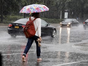 A woman tries to save her shoes as she gets caught in a brief but heavy downpour in Montreal on Monday July 31, 2017.