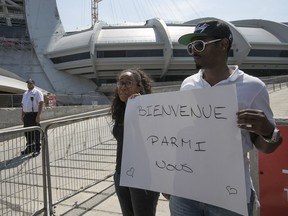 Naomi Jolicoeur and Max LeGrande stand outside the Olympic Stadium with a sign to welcome Haitian refugees arriving by bus at the facility on Wednesday, Aug. 2, 2017.