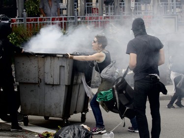 Counter-protesters wearing masks push a smoking trash bin as another counter-protester tries to stop them in a demonstration against far-right group La Meute Sunday, August 20 in Quebec City.