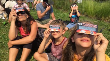 Halos Krastev and her children Alex and Emilian test their eclipse-viewing cards at Olympic Park in Montreal on Monday, Aug. 21, 2017.