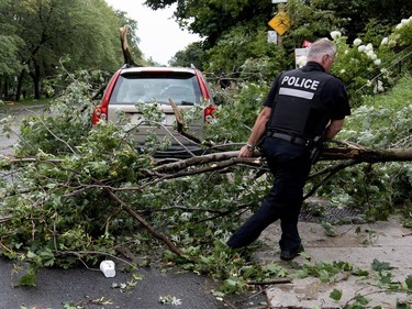 A police officer pulls damaged branches off of Girouard Ave. to reopen it to southbound traffic after a storm ripped through N.D.G. Park, damaging most trees in the park, in Montreal on Tuesday August 22, 2017.