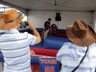 Ten-year-old Gad Seffour is watched by his parents as he tries bull riding at the rodeo in the Old Port of Montreal, Aug. 24, 2017.