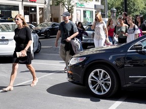 Pedestrians walk around a car that was forced to stop in the crosswalk after jaywalkers kept her from making a southbound turn on Peel Street in Montreal on Monday August 28, 2017.