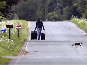 Dulne Brutus of Haiti tows his luggage down Roxham Road in Champlain, N.Y., while heading to an unofficial border station across from St-Bernard-de-Lacolle on Aug. 7, 2017. Officials on both sides of the border first began to notice last fall, around the time of the U.S. presidential election, that more people were crossing at Roxham Road. Since then, the numbers have continued to climb.