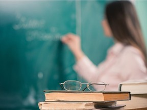 Glasses and books at the classroom table while teacher writing on a blackboard.