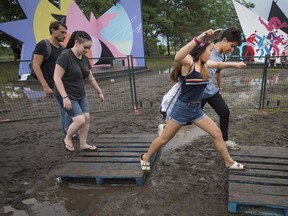 Music fans make the best of a couple wood pallets to cross a mud covered field during the Osheaga Music and Arts Festival at Parc Jean Drapeau in Montreal on Friday, August 4, 2017.