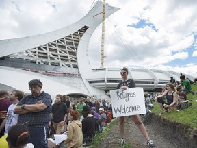 People hold up signs in support of asylum seekers during a rally outside the Olympic Stadium in Montreal, Sunday, August 6, 2017. The stadium is now being used as a temporary shelter for some of the hundreds of asylum claimants pouring across the New York-Quebec border every day.
