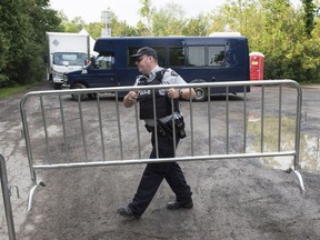 An RCMP officer moves a barricade as they wait for the arrival of asylum seekers crossing the border into Canada from the United States near Hemmingford Aug. 3, 2017.