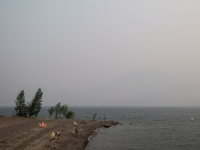 Thick smoke from wildfires fills the air as people stand on a beach on Kamloops Lake west of Kamloops, B.C. Quebec is sending reinforcements to help battle the wildfires on the west coast.