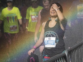 With a water hose creating a rainbow, Luz Fernandez, tries to cool down after taking part in the half-marathon in Montreal on Sunday, Sept. 24, 2017.