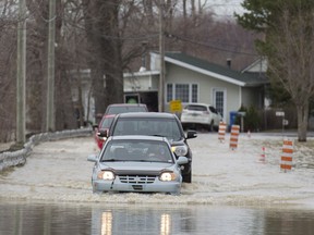 Cars move along a street in the town of Rigaud, west of Montreal, on Thursday, April 20, 2017, following flooding in the area.