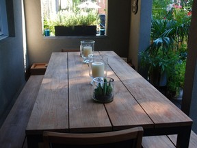 The backyard of Katie Bridgman's home, which features an inviting rectangular wooden table adorned with green succulent plants and hurricane lanterns.