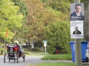 A man rides by election posters of Beaconsfield mayoral candidates Georges Bourelle and James Bonnell in Beaconsfield on Oct. 6.