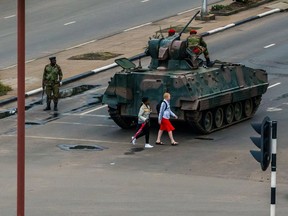 Young women walk past an armoured personnel carrier that stations by an intersection as Zimbabwean soldiers regulate traffic in Harare on November 15, 2017. Zimbabwe's military appeared to be in control of the country on November 15 as generals denied staging a coup but used state television to vow to target "criminals" close to President Mugabe.