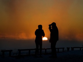 A couple watch the sun set on 2017 at the pier in Lachine, west of Montreal, on Sunday, Dec. 31, 2017.