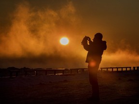A man takes pictures as the sun sets on 2017 at the pier in Lachine, west of Montreal on Sunday, Dec. 31, 2017.