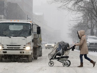 A woman pushes a baby stroller across Ste-Catherine St. during a snowstorm in Montreal Dec. 12, 2017.