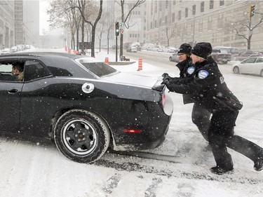 Montreal police officers help push a car during the city's first big snowstorm of the season Dec. 12, 2017.