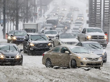 Motorists drive around a car that didn't have enough traction to make it up Robert-Bourrassa Blvd. at de la Gauchetiere St. during a Montreal snowstorm Dec. 12, 2017.