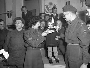 Corporal M. Freeman, Canadian Women's Army Corps (C.W.A.C.), and Captain Samuel Cass, Jewish chaplain, presenting a gift to a Belgian girl during a Hanukkah celebration, Tilburg, Netherlands, Dec. 17, 1944.