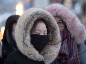 Jessica Wong, of China, covers her face as she walks Sainte-Catherine Street with friend Elaine Yu as Montreal enters a cold snap on Wednesday December 27, 2017.