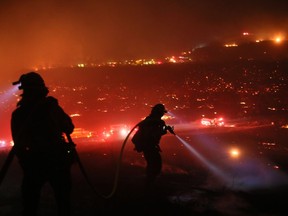 Firefighters walk to the fire line at the Lilac fire in Bonsall, California on December 7, 2017. Local emergency officials warned of powerful winds on December 7 that will feed wildfires raging in Los Angeles, threatening multi-million dollar mansions with blazes that have already forced more than 200,000 people to flee.