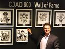 Broadcaster Andrew Carter holds up a caricature of Aislin from recently retired CJAD host Tommy Schnurmacher, the radio station's latest Wall of Fame inductee.  Caricatures of past members on the wall are from top left: George Balcan, Gord Sinclair, Ted Blackman, Dave Fisher, and Paul Reid.