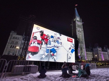 Children sit below a screen on Parliament Hill's west lawn showing the Ottawa Senators and Montreal Canadiens playing the NHL 100 Classic at nearby Landsdowne Park, in Ottawa, Saturday, Dec. 16, 2017.