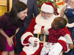 A young boy sits on Santa's knee as Montreal mayor Valérie Plante looks on during an open house at city hall in Montreal, Saturday, December 23, 2017.