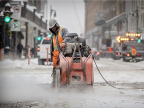 A construction worker saws through the asphalt on Ste-Catherine St. at Union in Montreal Jan. 8, 2018.