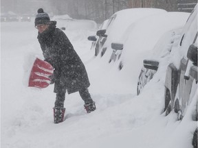 Lorraine Brooke tries to clear the snow away from her car on St-Antoine St. W. near Laporte Ave. in Montreal on Saturday, January 13, 2018.